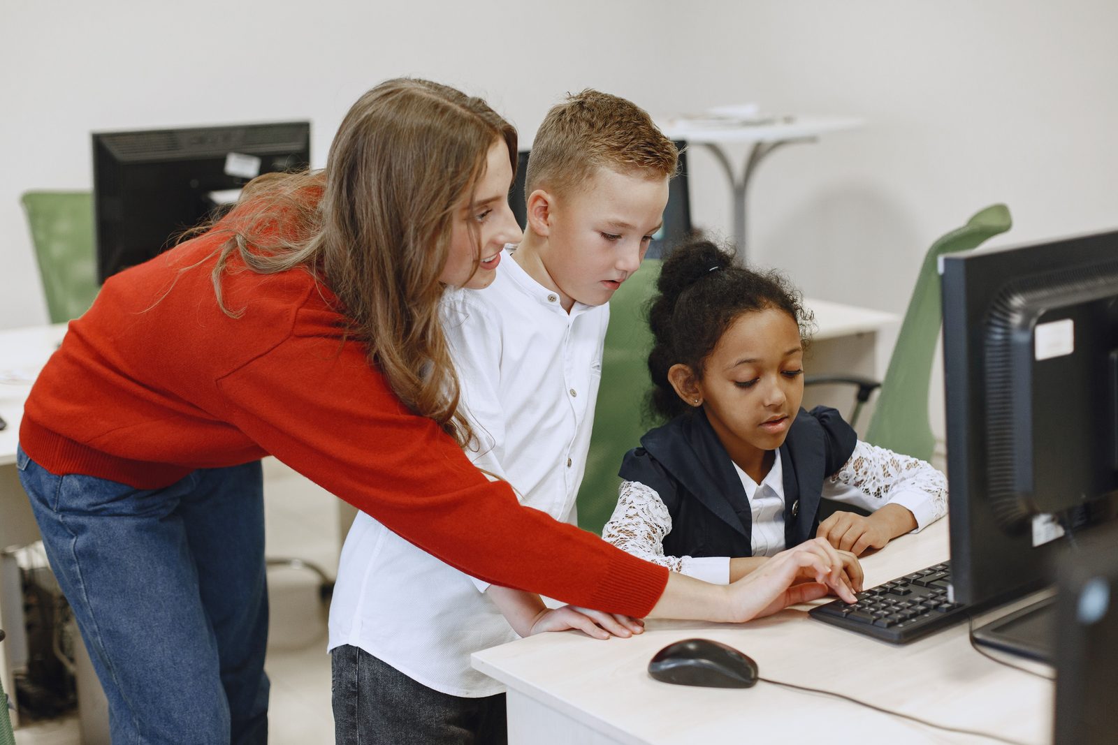 A teacher guiding two young students at a computer